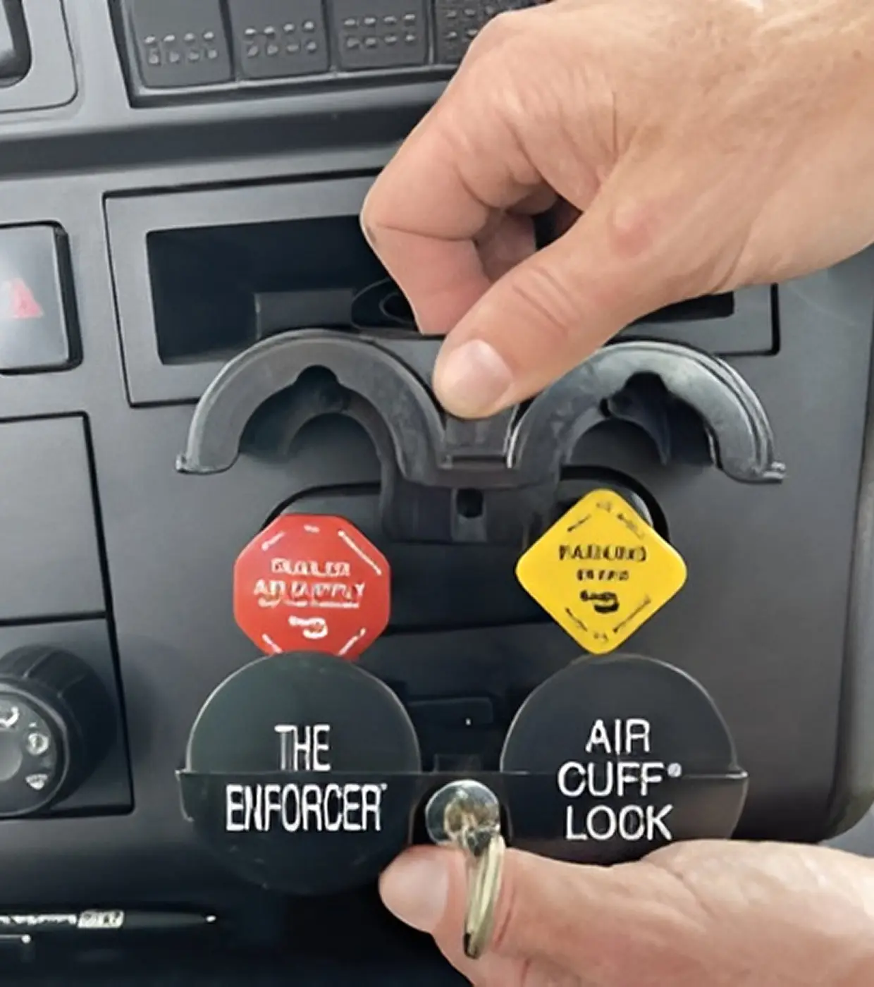 A person places a locking device labeled "The Enforcer" over the trailer air supply and parking brake knobs of a vehicle.