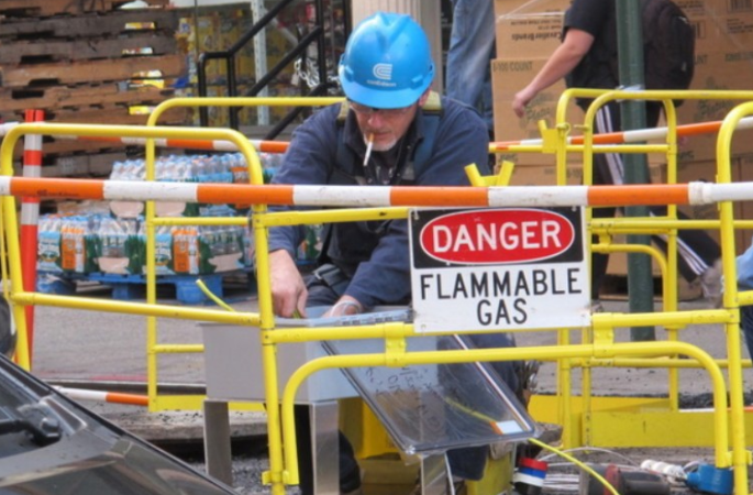 Worker near flammable gas sign, smoking cigarette.